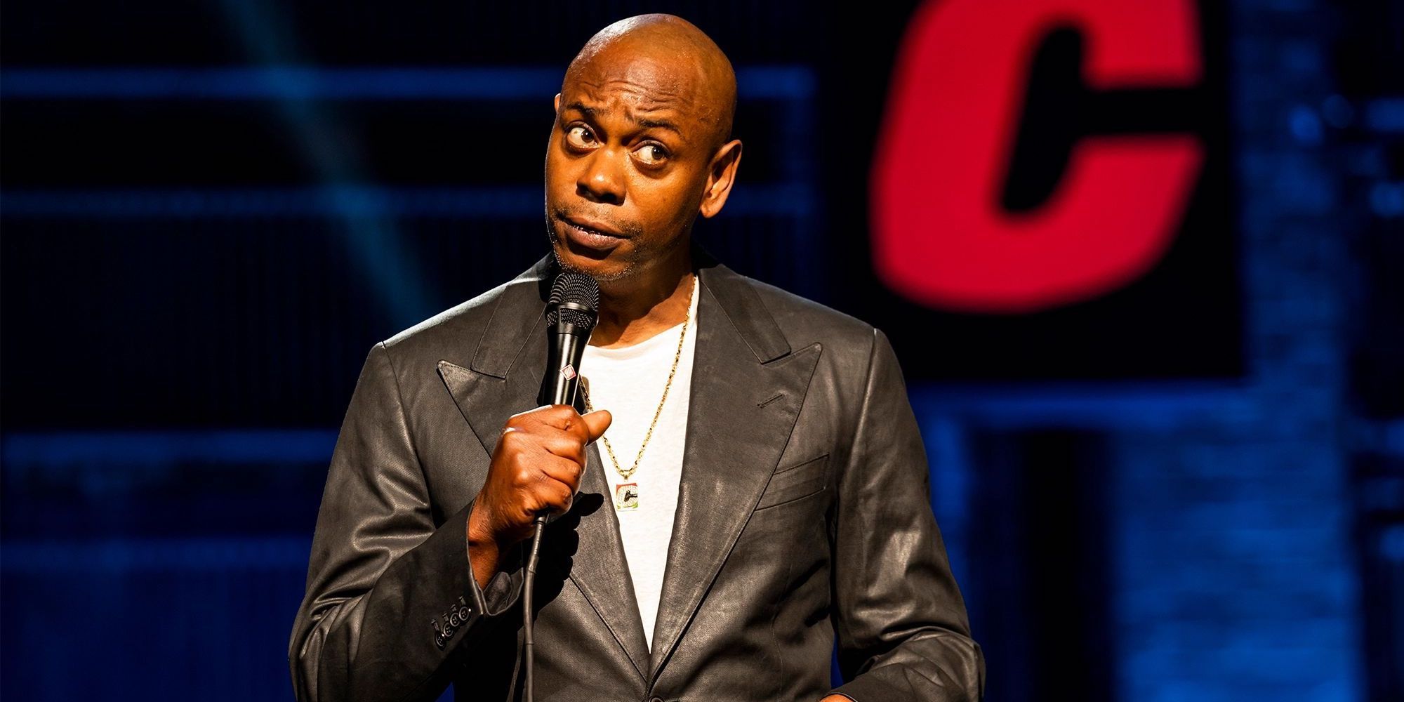 Dave Chappelle standing on stage and holding a microphone.