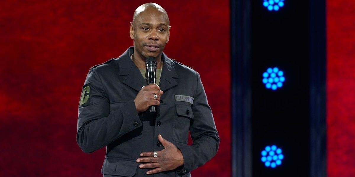 Dave Chappelle holding a microphone and standing on stage.