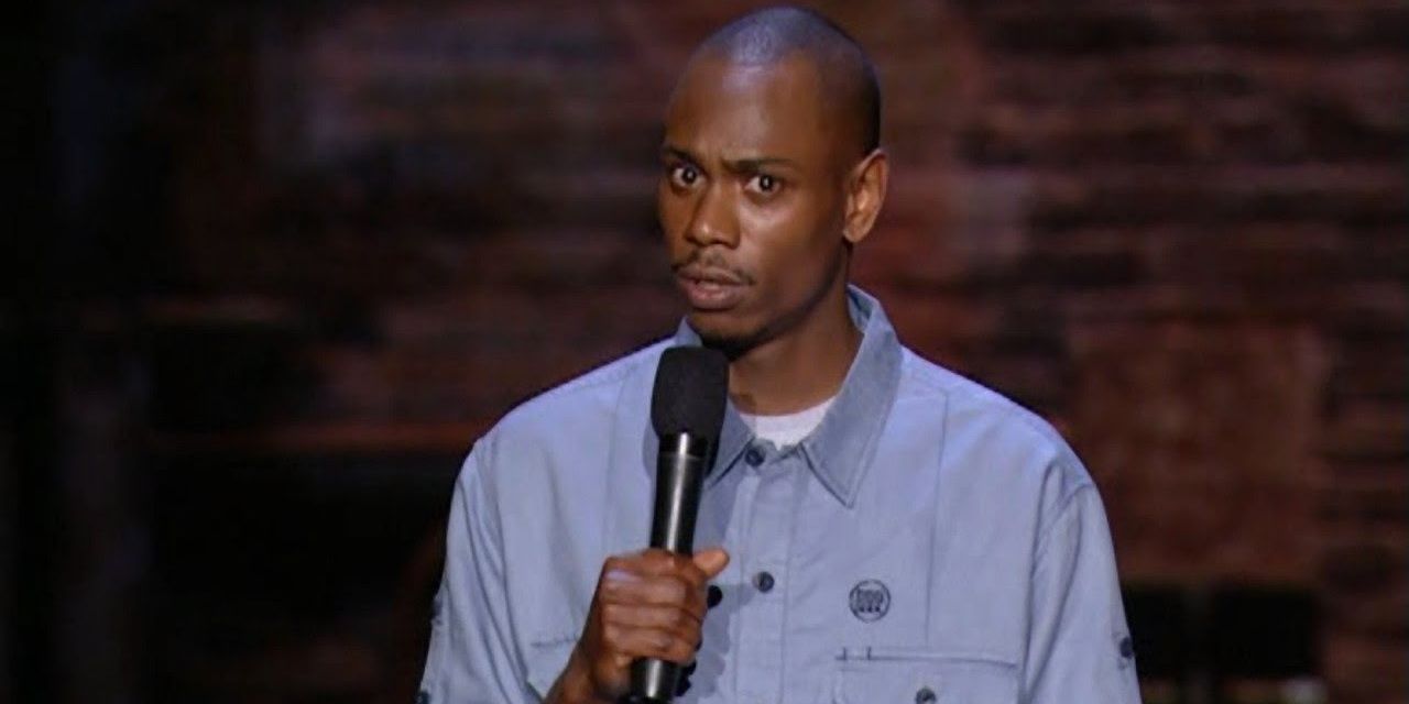 Dave Chappelle standing on stage and holding a microphone.